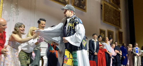 Kober runs across the stage with his hand out as others reach their hands out to touch his.