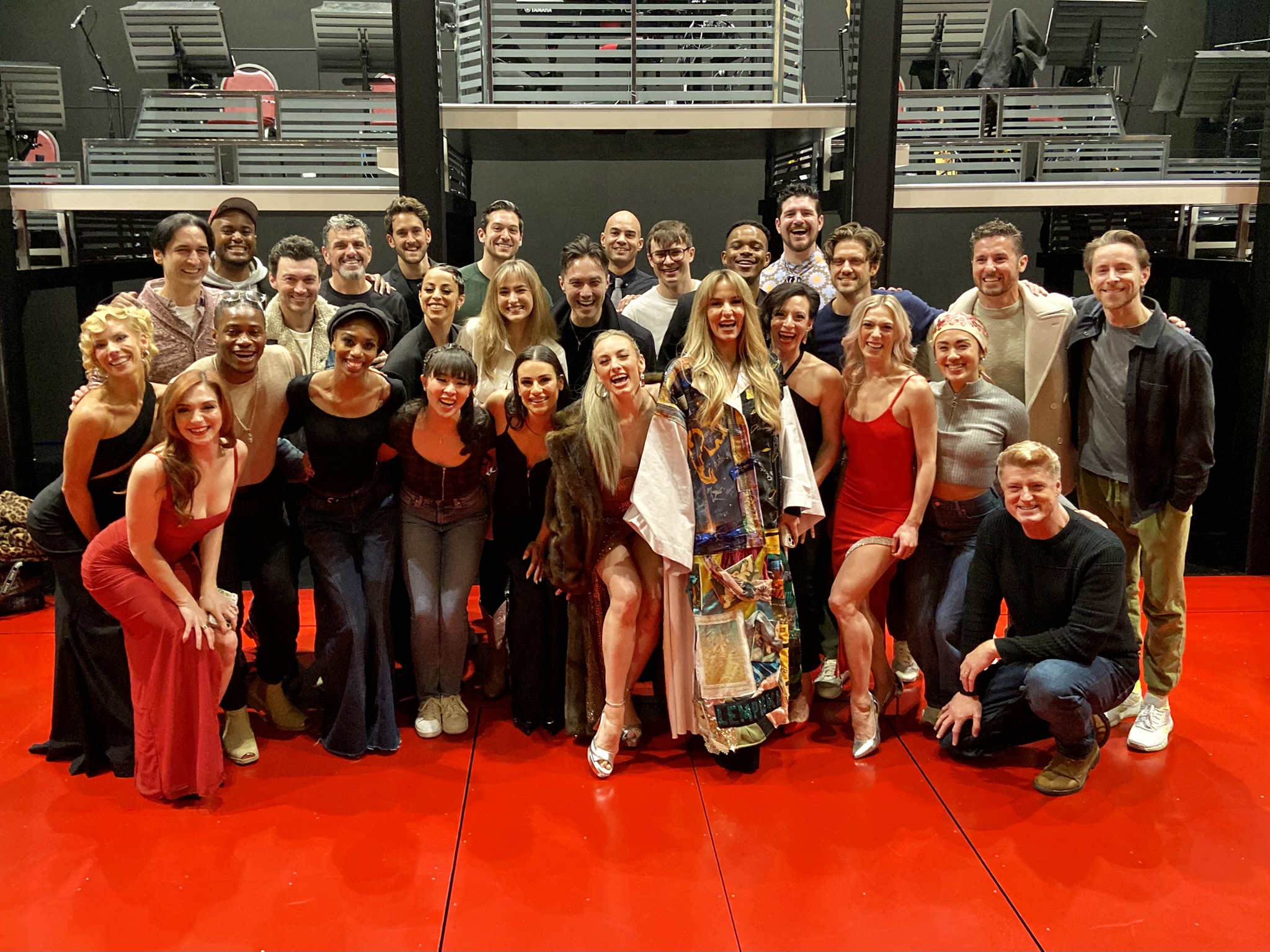 Webber stands onstage wearing the Robe, surrounded by about 27 posing castmates.
