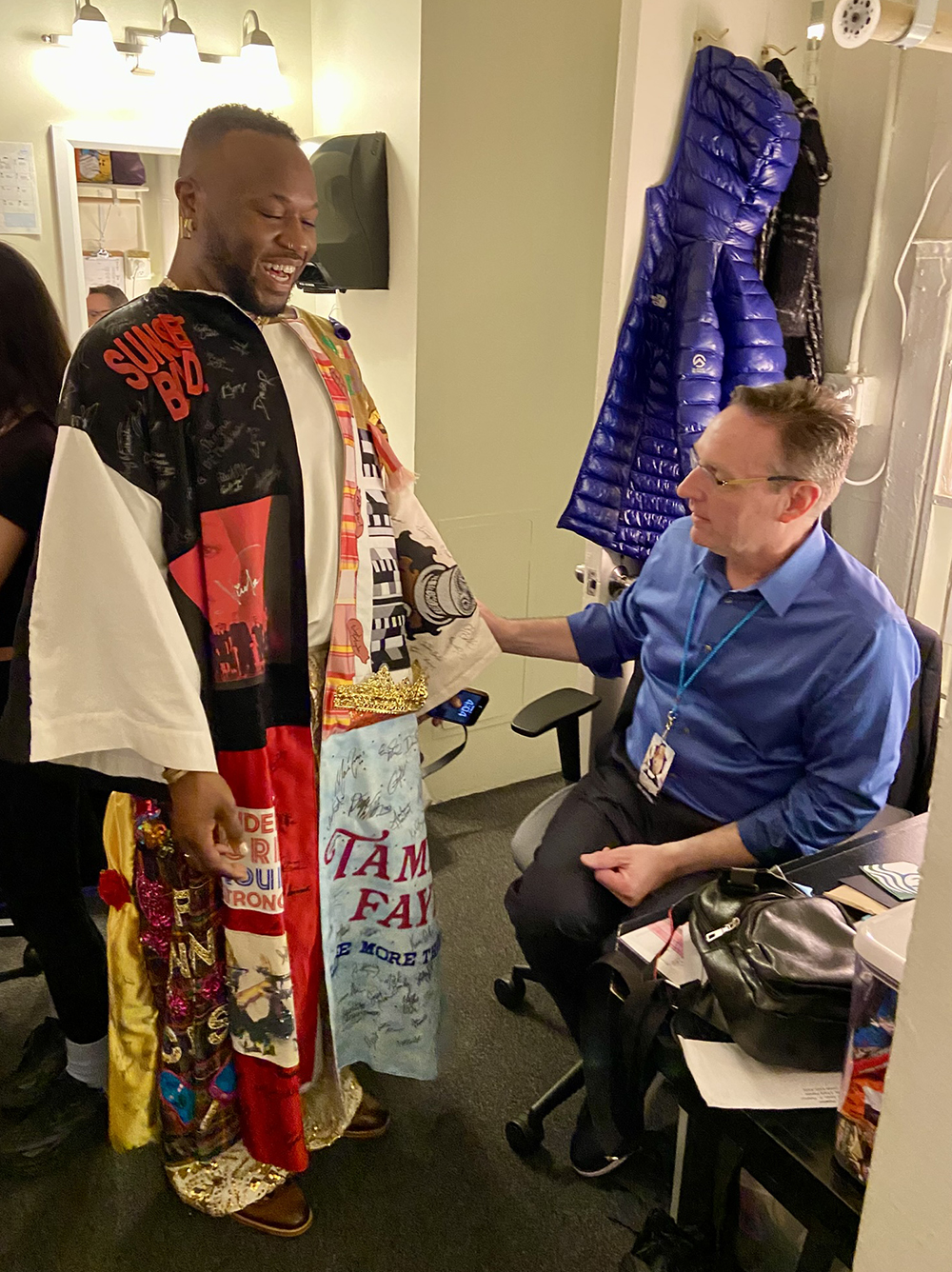Polanco Jones, Jr. stands in the Robe next to Rick Steiger who is seated in an office chair.